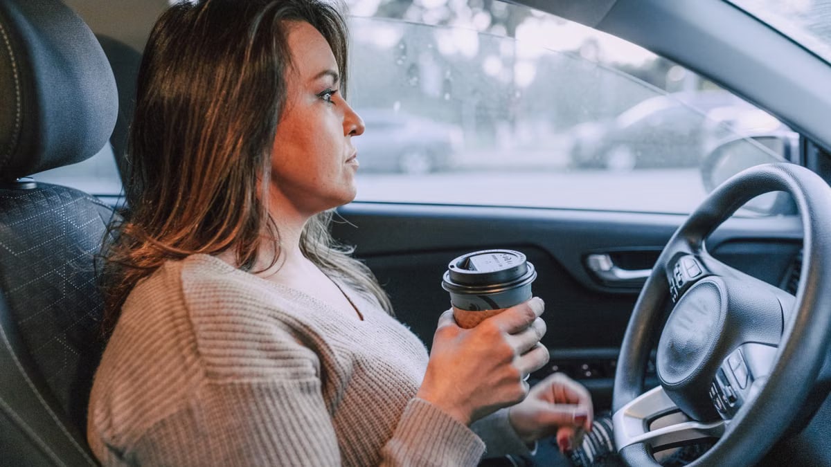 A woman in a car holding a disposable coffee cup, showing focus.